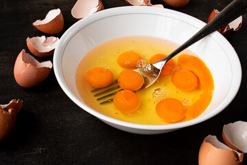 Close-up view of raw egg yolks and whites in a bowl with a fork, surrounded by cracked shells, symbolizing cooking preparations and homemade meals.