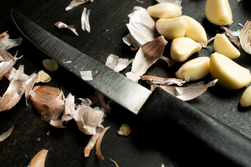 Garlic cloves and bulb arranged on a kitchen countertop with a knife, emphasizing cooking and ingredients. 