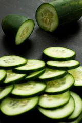 Close-up of sliced fresh cucumbers arranged on a dark background highlighting their texture and freshness, copy space.