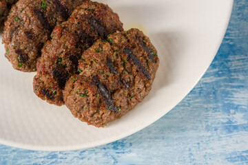 Grilled meatballs on a white porcelain plate on a blue stone table