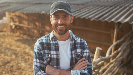 Front camera view of bearded Caucasian male fixing his hat with one hand. Looking into distance. Holding rakes with one hand. Wearing checkered shirt. Smiling. Finishing hard working day at farm. © VAKSMANV