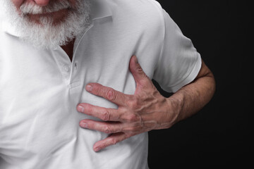 Heart attack. Senior man suffering from pain in chest on black background, closeup
