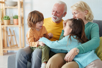 Obraz premium Caucasian Grandparents Enjoying Quality Time With Young Grandchildren Laughing Together On Living Room Sofa