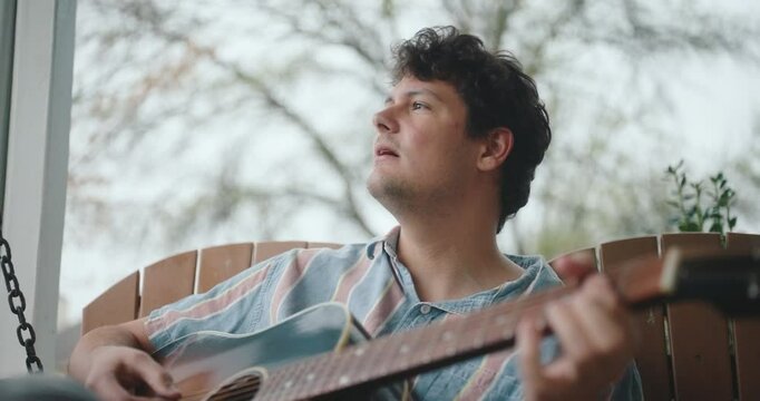 Young male musician sitting on a porch, playing guitar and writing a song