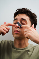 Young guy applying charcoal nose strip for deep nose pores cleaning. Male beauty and skincare...