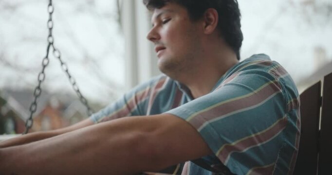 Young male musician sitting on a porch, playing guitar and writing a song