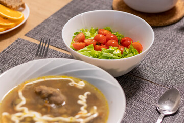 Bawl with cherry tomatoes and lettuce leaves, bawl with soup next to it. Food
