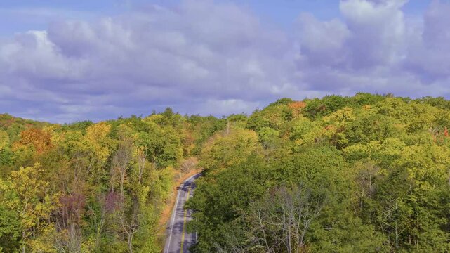 This stunning 4K drone shot shows Canopus Lake with sunlight on the autumn forest and a road passing beside the lake, all under soft cloudy skies.