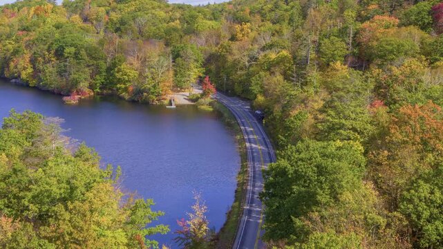 Captured in 4K, this footage shows Canopus Lake in Kent, NY, with sunlight filtering through autumn trees beside the lake and a road running alongside it.