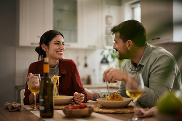 Happy couple talking while eating spaghetti for lunch at home.