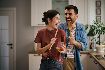 Carefree couple singing and having fun wile cooking in the kitchen.