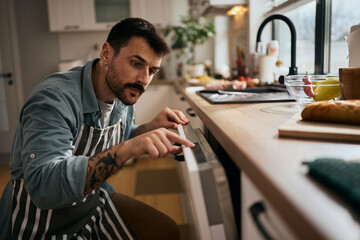 Mid adult man using dishwasher while doing the dishes in the kitchen.