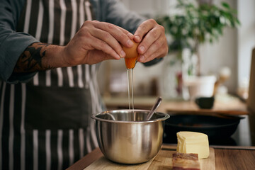 Close up of man cracking an egg while preparing food in the kitchen.
