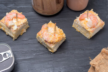 Prawn canape on black slate tray on wooden table with jars and cans of preserves