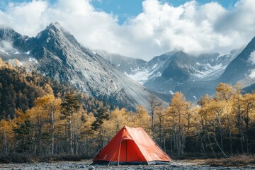 Red tent in a forest clearing. Tourist tent against background of autumn trees and mountains.
