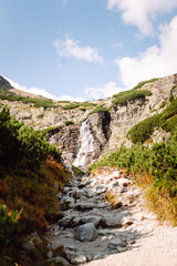 Natural mesmerizing scenery. A tall waterfall flows over the rocky cliffs in the mountains. Picturesque scenery and lush vegetation. The concept of nature, beauty.