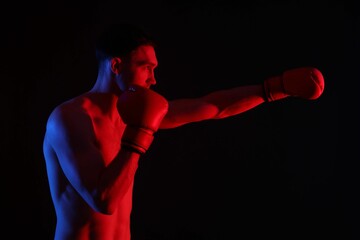 Man in boxing gloves fighting on black background in neon lights