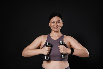 Fototapeta premium Plus size woman in gym clothes doing exercise with dumbbells on black background