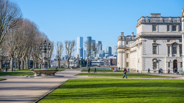Visitors stroll through the beautifully landscaped grounds of the Old Royal Naval College in Greenwich. The stunning architecture contrasts with the modern skyline in the background.