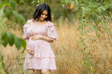 Beautiful brunette pregnant woman walks in the park at sunset in summer
