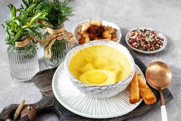 A bowl of homemade chicken broth with eggs and crusty bread served on a rustic wooden board