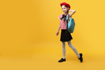 Schoolgirl with beret and backpack on yellow background. Space for text