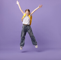 Stylish schoolgirl with backpack jumping on violet background