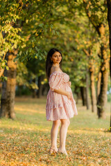 Beautiful brunette pregnant woman walks in the park at sunset in summer