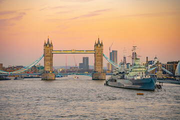 Fototapeta premium The iconic Tower Bridge stands majestically over the Thames River as HMS Belfast rests nearby. The evening sky glow envelops London, creating a picturesque scene.