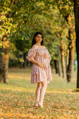 Beautiful brunette pregnant woman walks in the park at sunset in summer