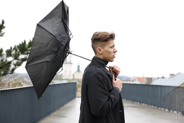 Man with broken umbrella fighting wind under rain outdoors