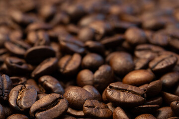 A rich, close-up macro shot of roasted coffee beans with a shallow depth of field, emphasizing the texture, detail, and oily surface of the beans. The blurred background enhances focus on the foregrou
