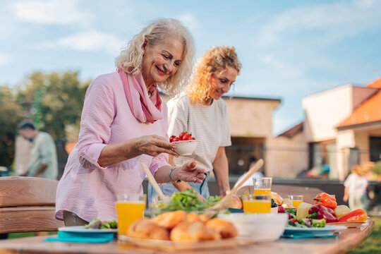 Senior woman enjoying garden party with family, preparing food on table