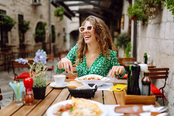 Beautiful tourist in bright green dress enjoying meal outdoors in cafe. Young woman having lunch in cafe in old town. Food and consumption concept, tourism.