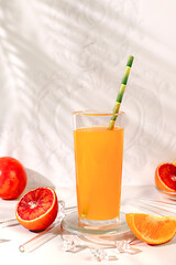 Modern still life with citrus fruits, orange juice, oranges and blood orange on elegant kitchen table with long hard shadows. Minimal detox diet concept, summer vitamin drinks, selective focus
