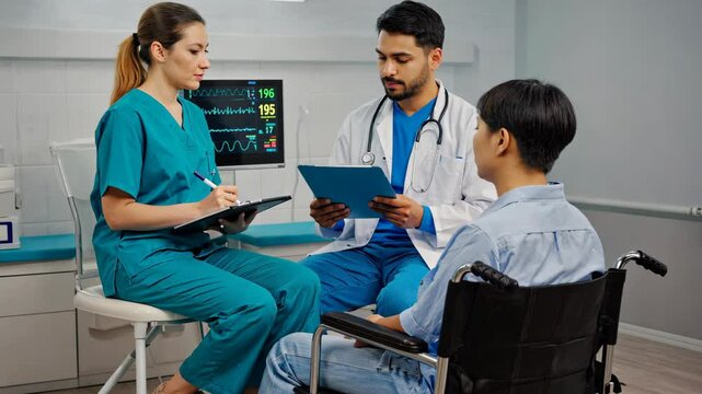 Doctor and nurse consulting with patient in wheelchair in examination room at a hospital, taking notes on healthcare