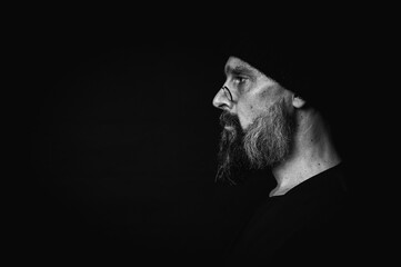 black and white, portrait, expressive mature man with sharp gaze and frowning face, wearing glasses and knitted hat, looking aside. Dramatic portrait with strong emotions on dark background, gaze.