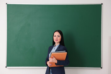 English teacher with books near chalkboard in classroom
