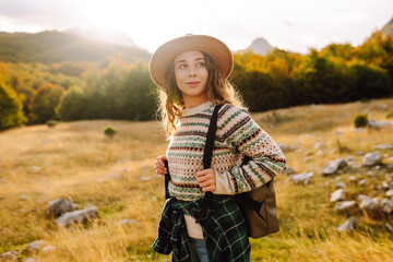 Woman traveler in hat feeling free, enjoying sunny weather in mountains on trail. Wanderlust....