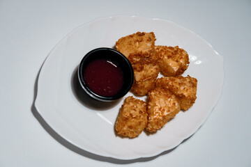 Crispy chicken nuggets with dark red berry sauce served on a white plate, top-down view isolated on white background