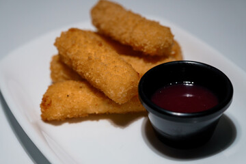 Crispy mozzarella sticks served with a dark red dipping sauce on a white rectangular plate, close-up view of appetizer
