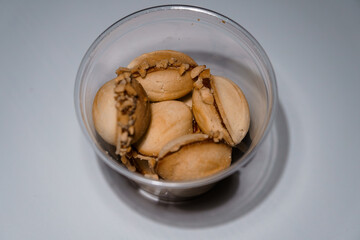 Heap of traditional fortune cookies with nut filling inside clear plastic container, top-down view on a white surface