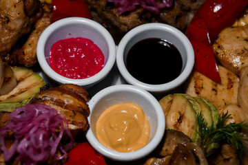 Close-up of a flavorful grilled meat platter with vibrant sauces, fresh vegetables, and colorful pickled onions presented on a dark background