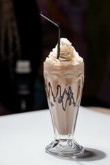 Delicious chocolate milkshake in a tall glass with whipped cream and chocolate drizzle, presented on a white surface, perfect for dessert or refreshment