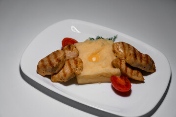 Grilled chicken with mashed potatoes and tomatoes served on a white rectangular plate, garnished with fresh herbs on a light background