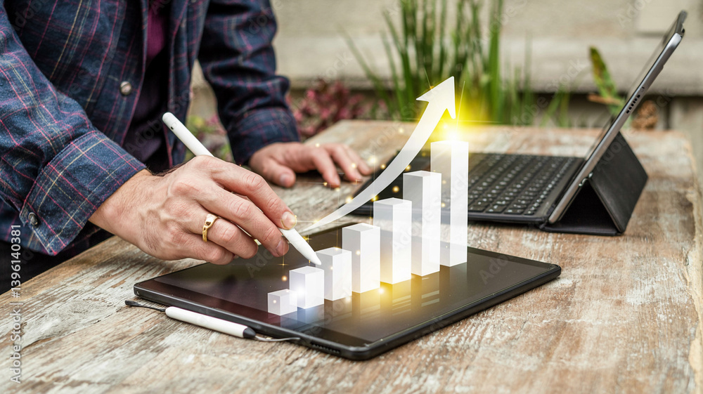 Aufkleber person using stylus on tablet with growth chart and laptop on wooden table in outdoor setting view