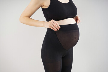 Young pregnant woman in black tights on grey background