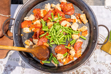 Chef adding green beans to paella with chicken and chorizo