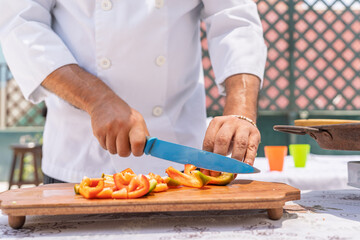 Chef slicing bell peppers outdoors for paella preparation