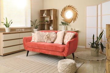Interior of modern living room with coral sofa, chest of drawers and stylish mirror